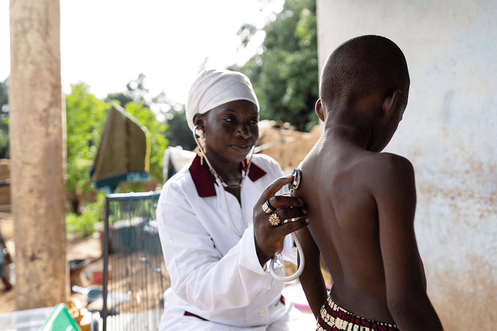 A South Sudanese midwife examining a child with a stethoscope at a rural clinic